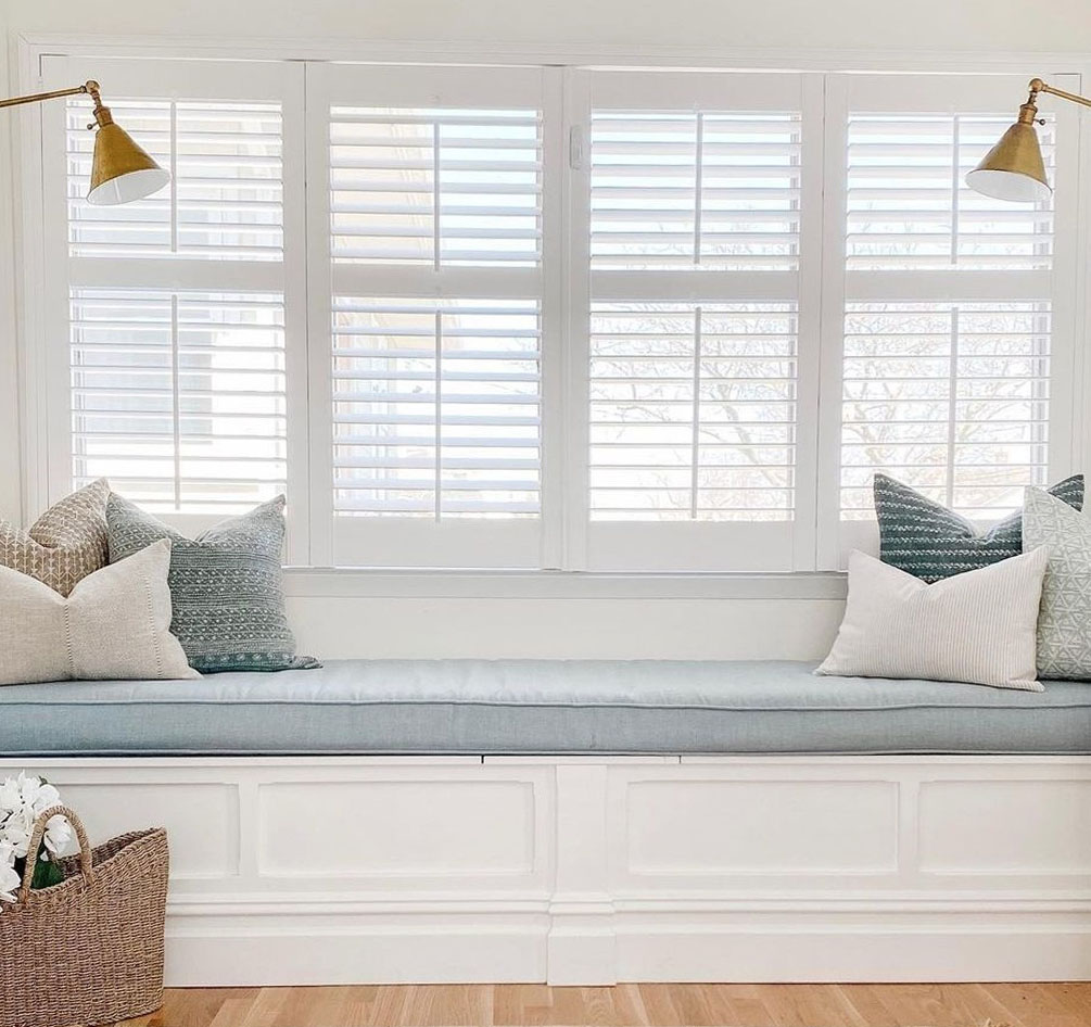 White polywood shutters by a window seat with lamps