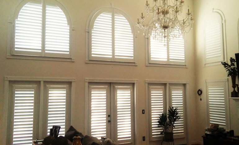 TV room in two-story Salt Lake City home with plantation shutters on arch windows.