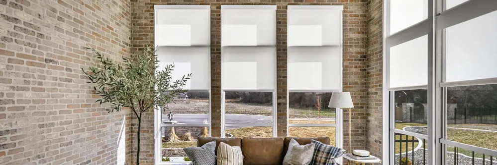 White motorized roller shades in a stylish living room with brick walls