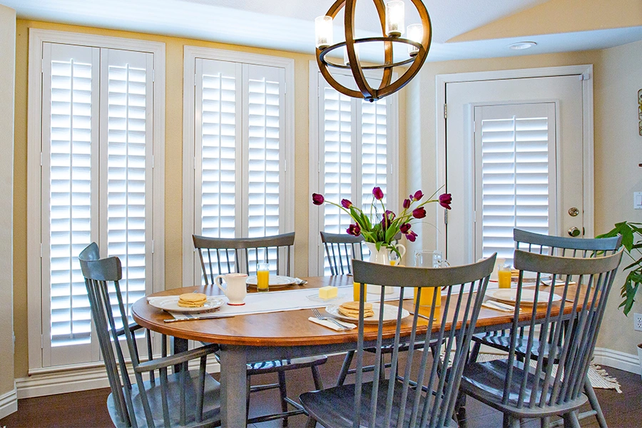 Keep your home cooler for less each summer when you install energy-efficient window treatments. White Polywood shutters on doors and windows in a kitchen eating nook