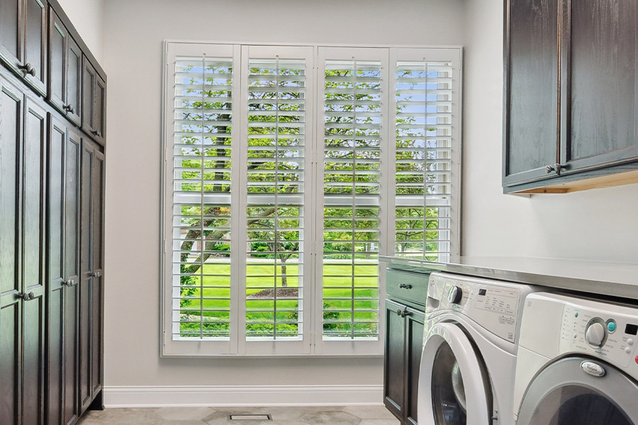Find the perfect level of natural light for your Salt Lake City laundry room with interior shutters. White Polywood shutters letting light through a laundry room window