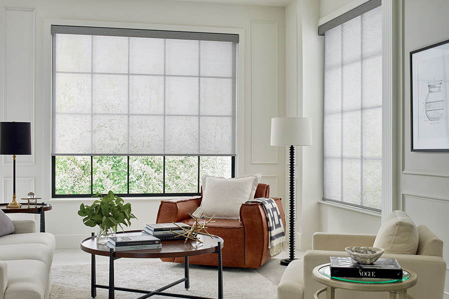 Sheer shades add texture and style to your living room. Light gray sheer shades on two large tall windows with a beige and tan styled living room.