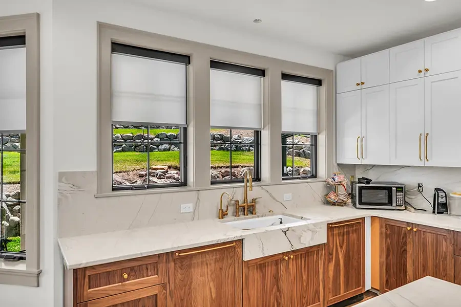 Slim roller shades offer modern appeal and require little window depth, making them a popular choice for small windows. Slim white roller shades on three windows in a kitchen